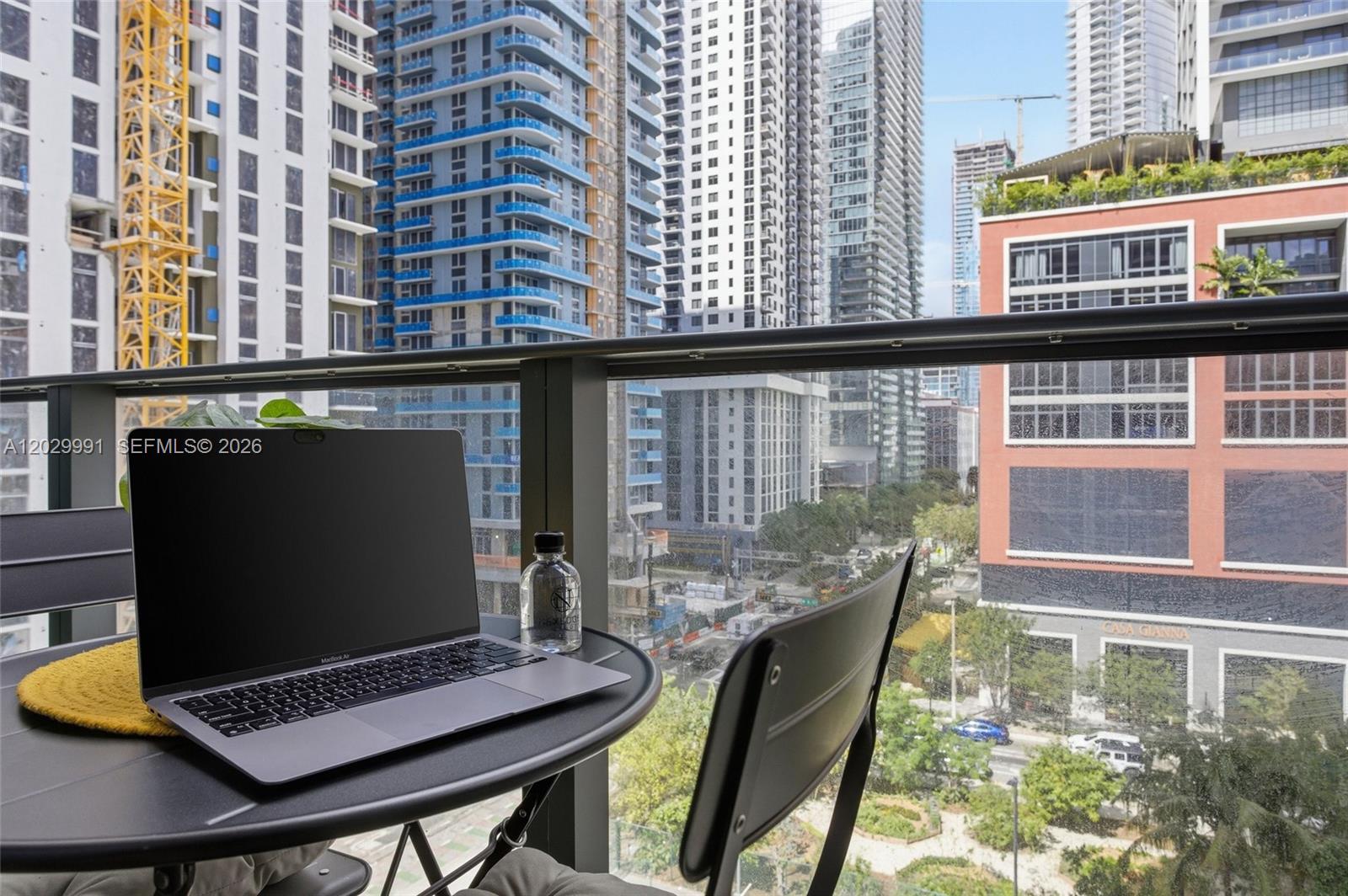 A laptop sits on a small balcony table overlooking a dense urban cityscape — 121 NE 5th St # 711, Miami FL 33132, MIAMI, FL