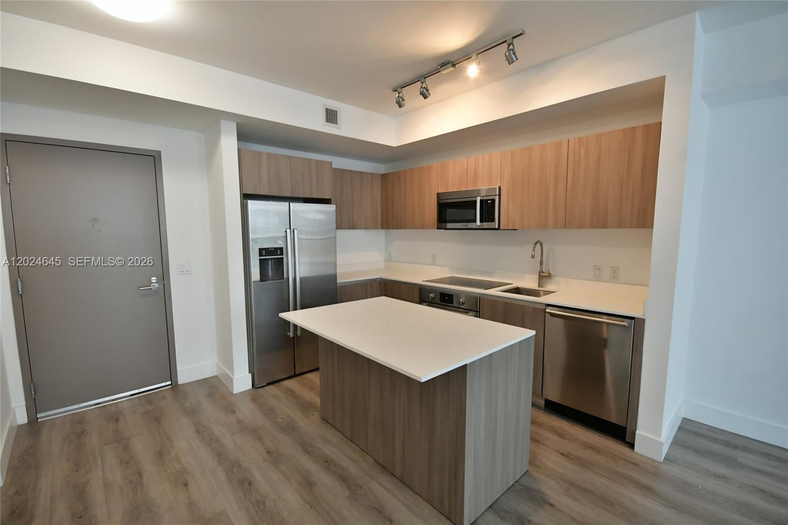 A modern kitchen features wood-grain cabinets, stainless steel appliances, and a white island countertop — 201 SW 17th Rd # 304, Miami FL 33129, MIAMI, FL