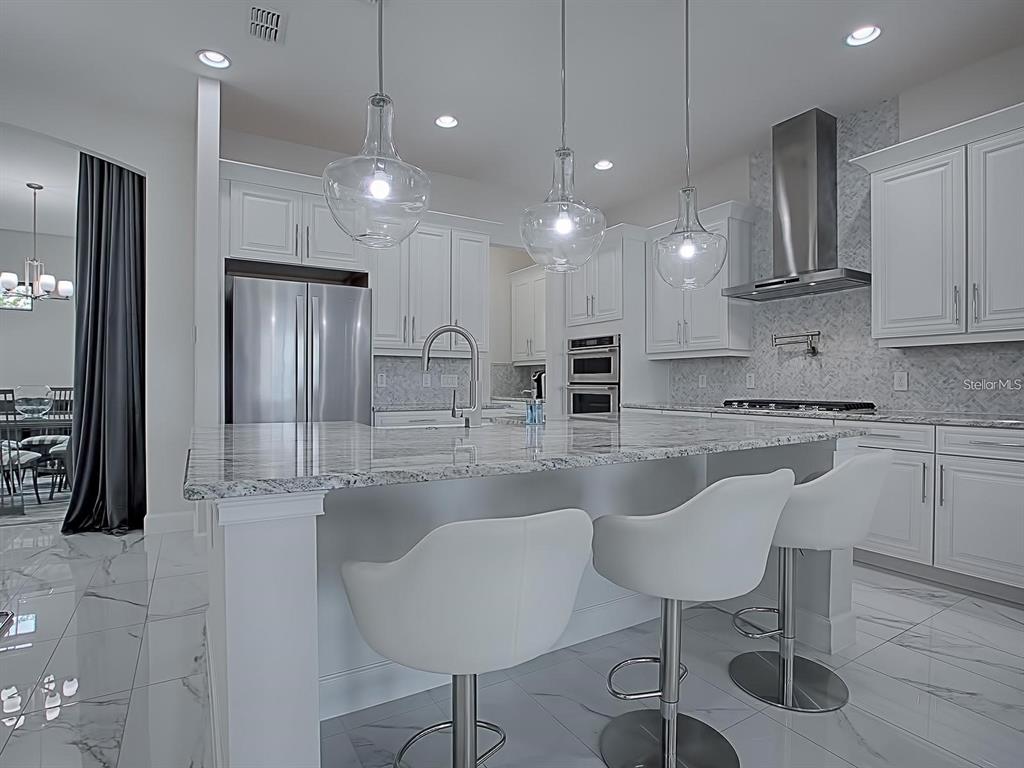 A modern kitchen features white cabinetry, a marble-topped island with bar stools, and stainless appliances — 7661 TOSCANA BOULEVARD, ORLANDO, FL