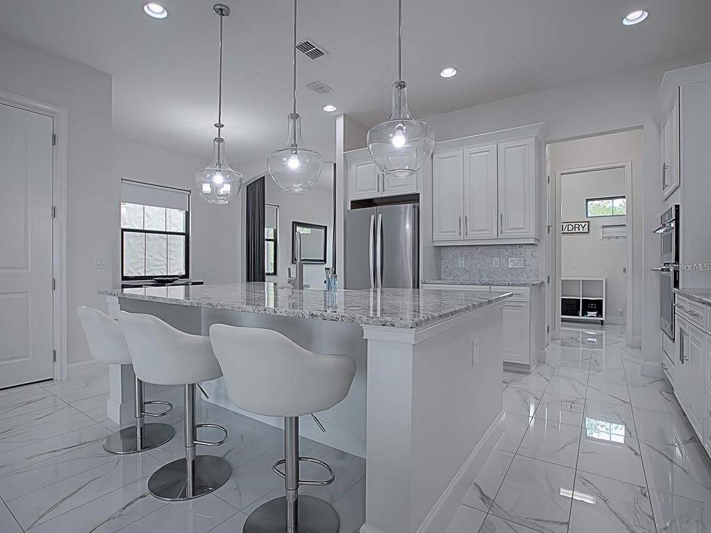 A modern white kitchen features a granite-topped island, pendant lighting, and polished marble-style flooring — 7661 TOSCANA BOULEVARD, ORLANDO, FL