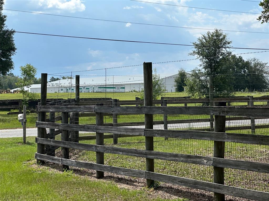 A wooden fence encloses a grassy field with a large industrial building in the background — 905 NW 80TH AVENUE, OCALA, FL