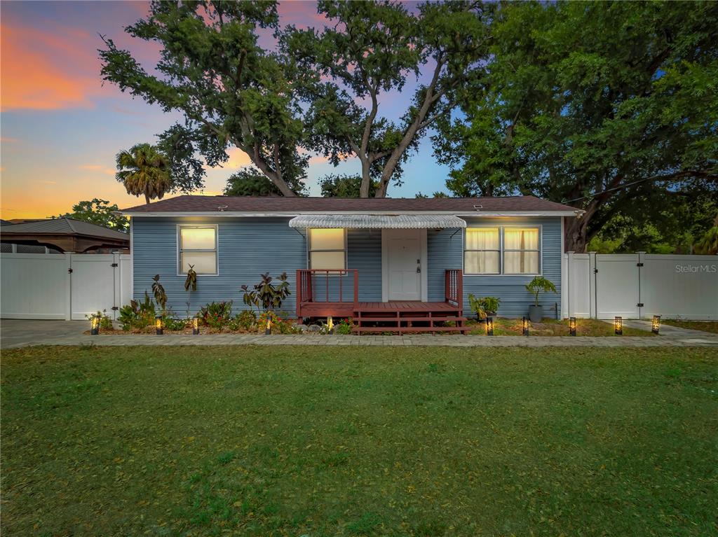 A blue single-story house with a wooden front porch and white vinyl fencing at dusk — 6201 THERESA STREET, TAMPA, FL