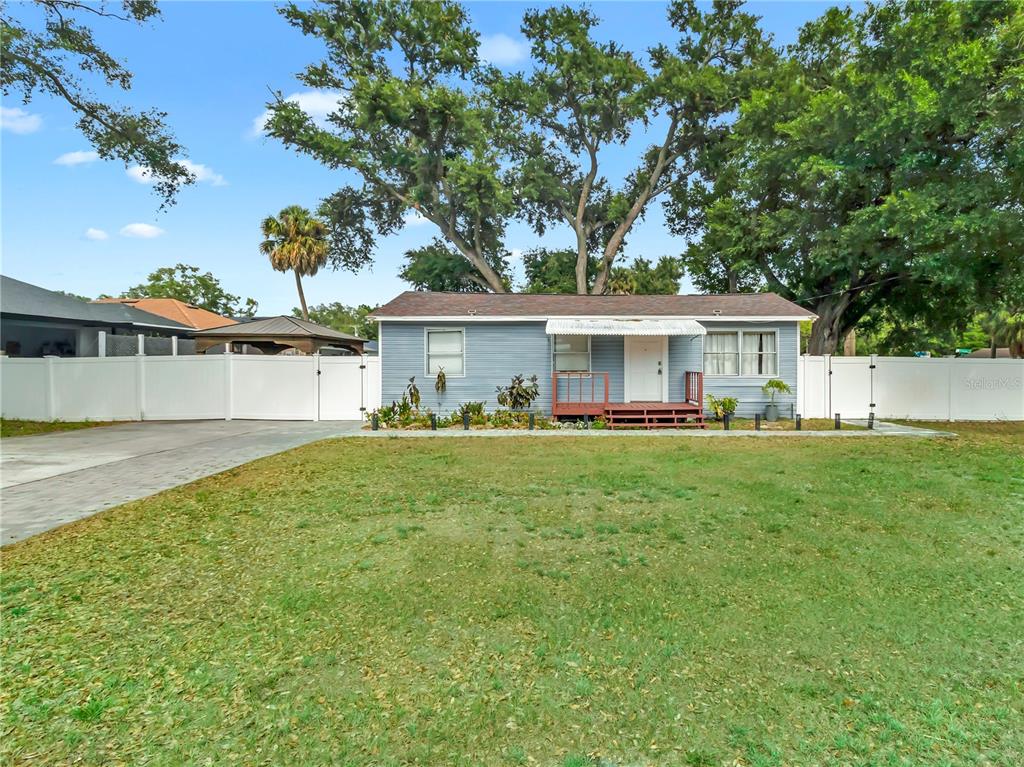 A single-story blue house with a front porch stands behind a large grassy yard — 6201 THERESA STREET, TAMPA, FL