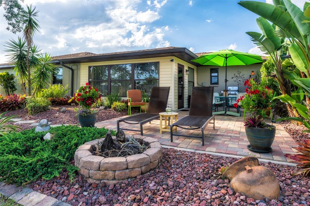 A backyard patio features a stone fire pit, two lounge chairs, and a green umbrella — 2360 BAL HARBOUR DRIVE, VENICE, FL