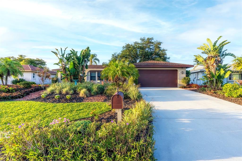 A single-story house with a brown garage door, a concrete driveway, and lush tropical landscaping — 2360 BAL HARBOUR DRIVE, VENICE, FL