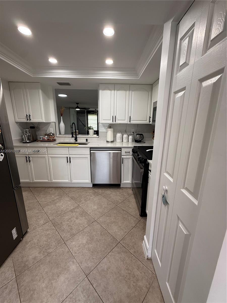 A kitchen features white cabinets, stainless steel appliances, a black stove, and tiled flooring — 1020 NW 80th Ave # 104, Margate FL 33063, MARGATE, FL
