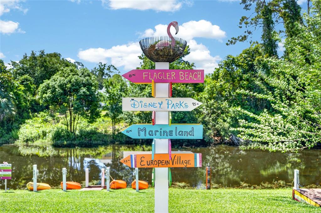 A wooden signpost with directional arrows sits on a lawn beside a pond — 36 FLAMINGO DRIVE, PALM COAST, FL