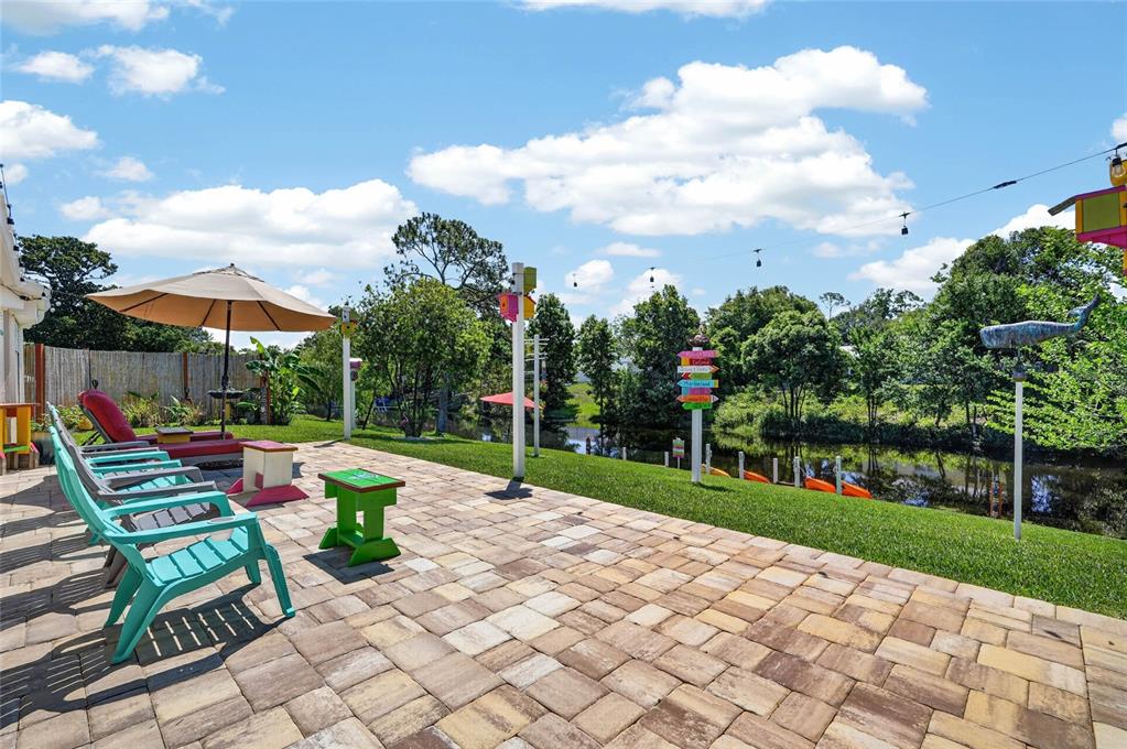 A paved patio overlooks a canal with colorful chairs, an umbrella, and decorative signage — 36 FLAMINGO DRIVE, PALM COAST, FL