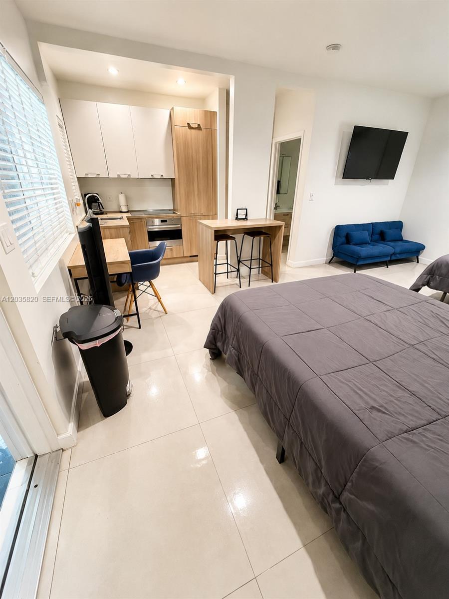 This studio apartment features a kitchenette, a dining island, a bed, and a blue sofa — 245 NE 33rd St # 104, Miami FL 33137, MIAMI, FL