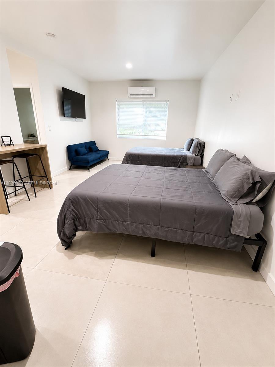 A bedroom features two beds, a blue sofa, a wall-mounted television, and tile flooring — 245 NE 33rd St # 104, Miami FL 33137, MIAMI, FL