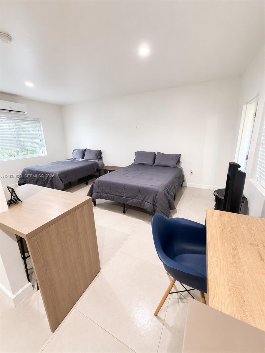 A bedroom features two beds with gray bedding, light tile floors, and two wooden desks — 245 NE 33rd St # 104, Miami FL 33137, MIAMI, FL