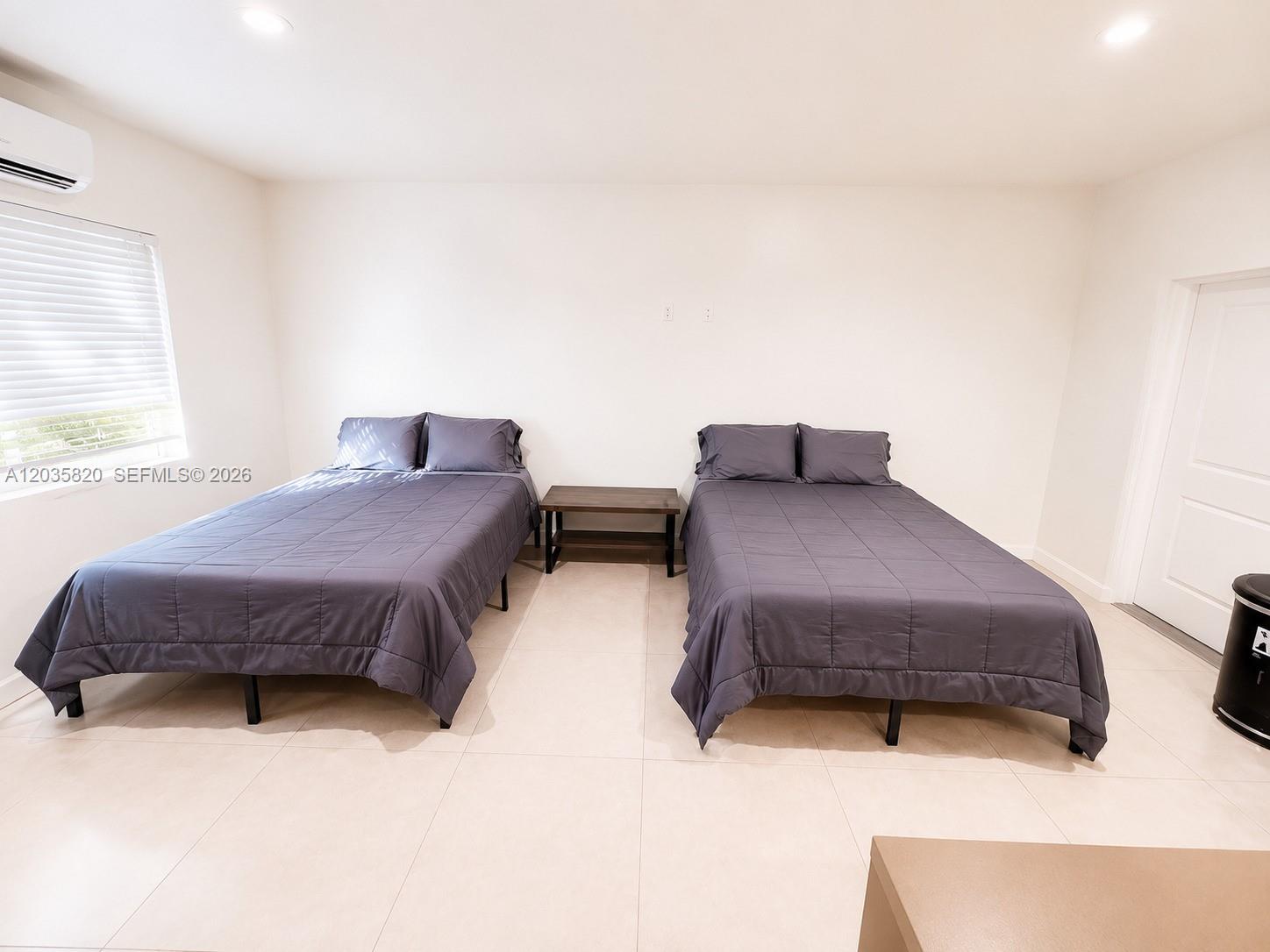 A bedroom features two beds with dark gray bedding separated by a small wooden table — 245 NE 33rd St # 104, Miami FL 33137, MIAMI, FL