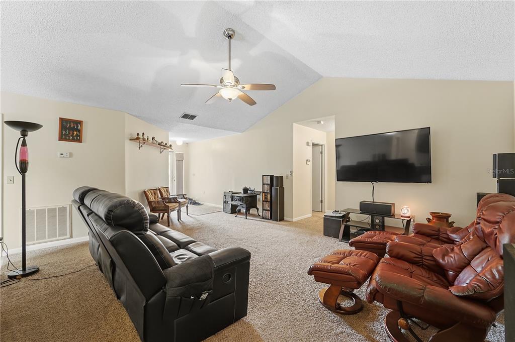 A living room with vaulted ceilings, beige carpet, a ceiling fan, and leather seating furniture — 358 N FORK PLACE, LAKELAND, FL