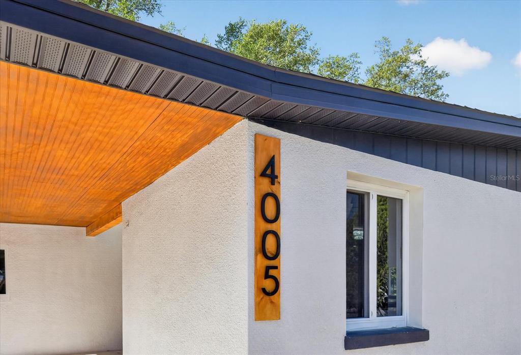 A vertical wooden plaque with the house number 4005 is mounted on a white stucco wall — 4005 E HENRY AVENUE, TAMPA, FL