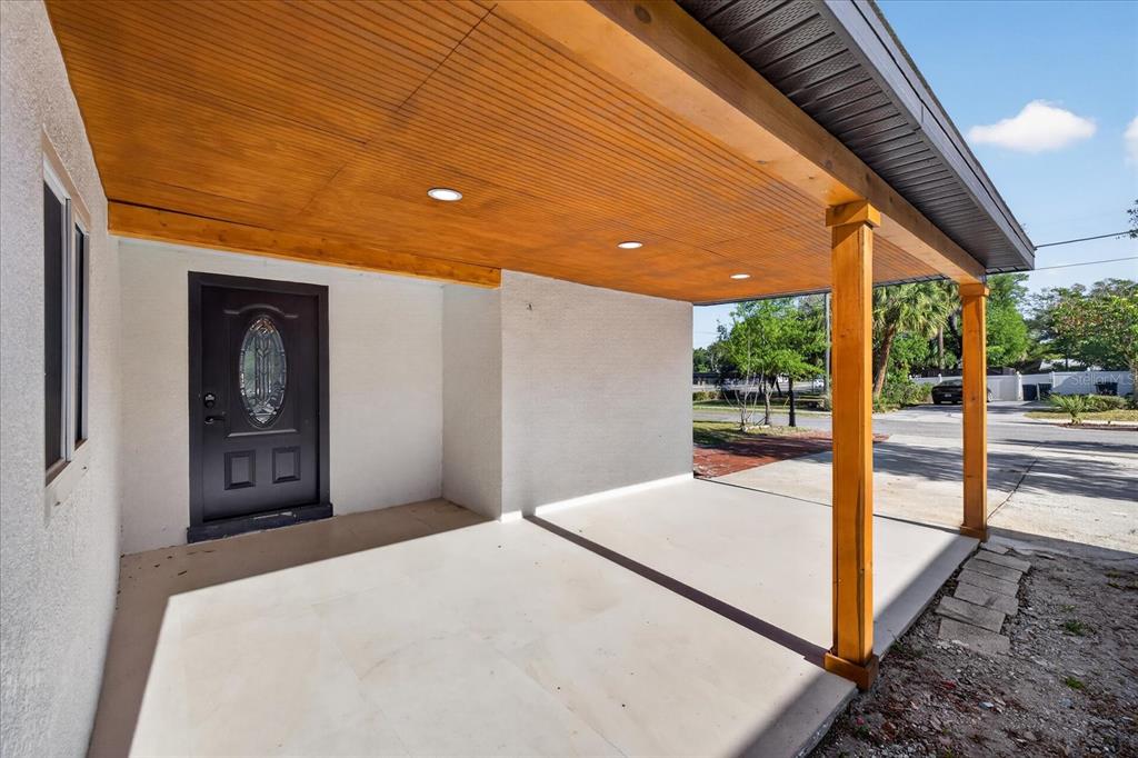 A covered concrete porch with a wood-paneled ceiling and a dark front door — 4005 E HENRY AVENUE, TAMPA, FL