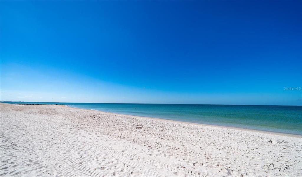 A wide, sandy beach meets the calm ocean under a clear, bright blue sky — 8200 BAYSHORE DRIVE UNIT 9, TREASURE ISLAND, FL