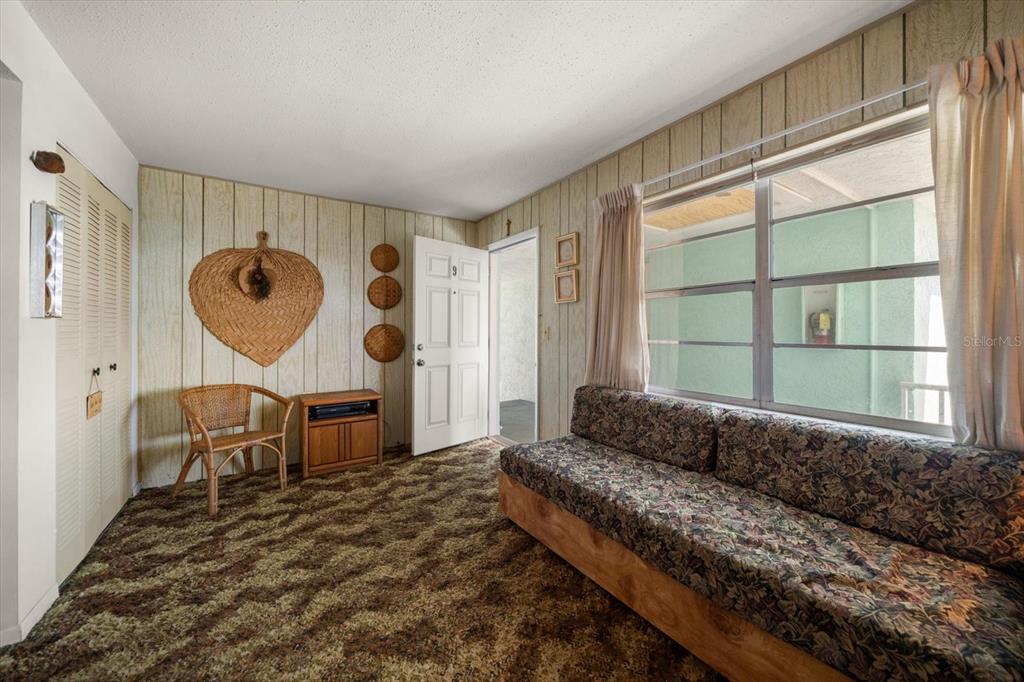 A living room features wood-paneled walls, patterned carpet, a floral sofa, and a wicker chair — 8200 BAYSHORE DRIVE UNIT 9, TREASURE ISLAND, FL
