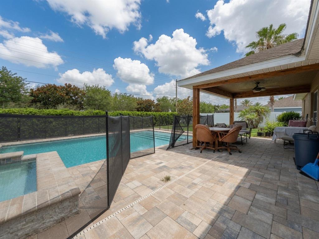 A backyard patio features a covered seating area, a swimming pool, and a safety fence — 233 MANDOLIN DRIVE, WINTER HAVEN, FL