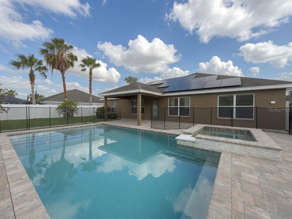 A backyard features a swimming pool, a raised spa, and a house with solar panels — 233 MANDOLIN DRIVE, WINTER HAVEN, FL