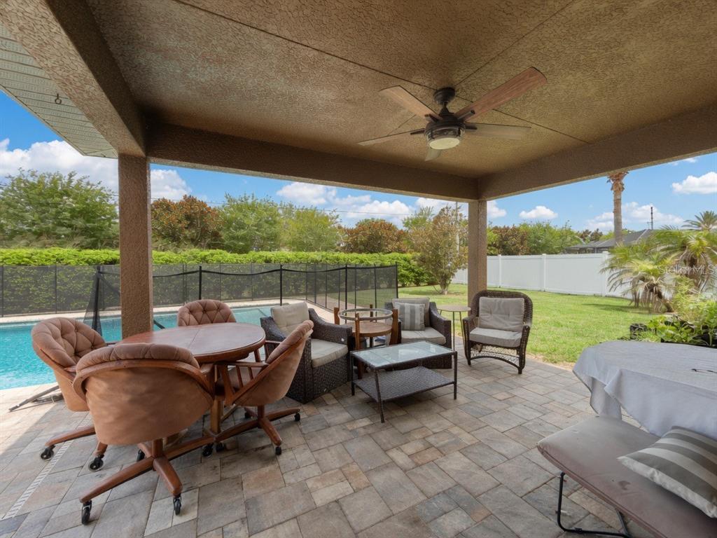 A covered patio features a ceiling fan, stone pavers, and outdoor furniture overlooking a pool — 233 MANDOLIN DRIVE, WINTER HAVEN, FL