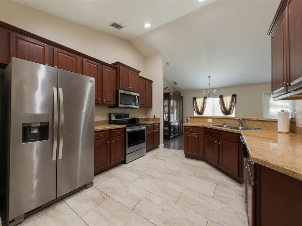 A kitchen with dark wood cabinets, stainless steel appliances, and tan granite countertops — 233 MANDOLIN DRIVE, WINTER HAVEN, FL