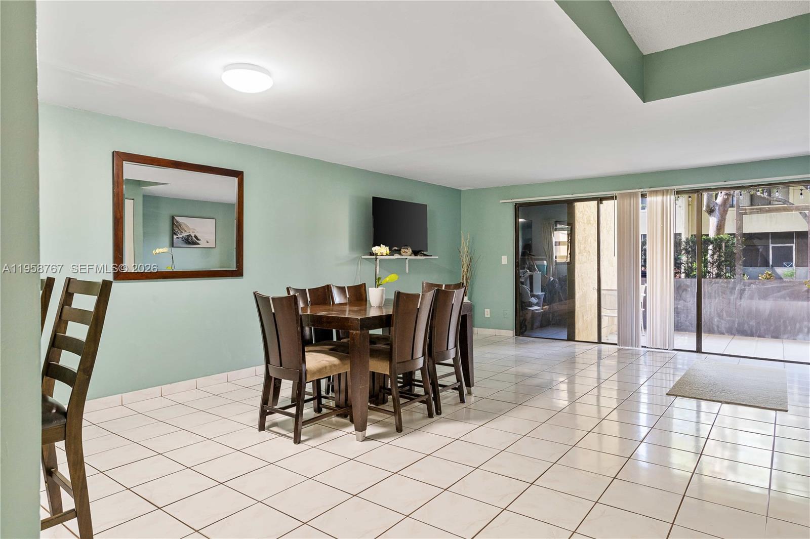 A dining area with a wooden table, chairs, tile flooring, and a wall-mounted television — 4713 N Pine Island Rd, Sunrise FL 33351, SUNRISE, FL