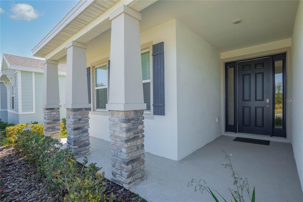 A front porch with stone-based columns leads to a dark blue front door — 7974 PENROSE PLACE, WILDWOOD, FL