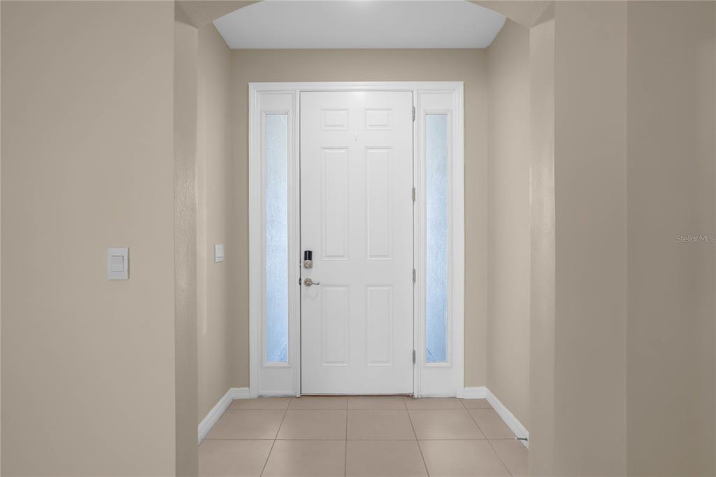A white front door with sidelights is centered in a neutral-toned entryway with tiled floors — 7974 PENROSE PLACE, WILDWOOD, FL