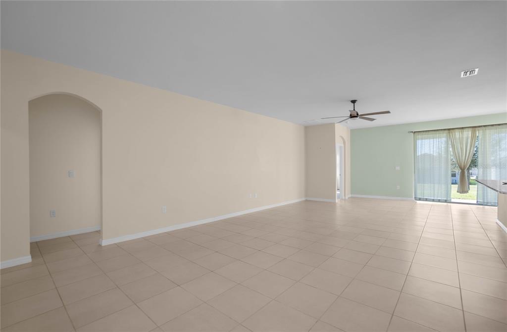 An open-concept living area features beige walls, light tile flooring, and a sliding glass door — 7974 PENROSE PLACE, WILDWOOD, FL
