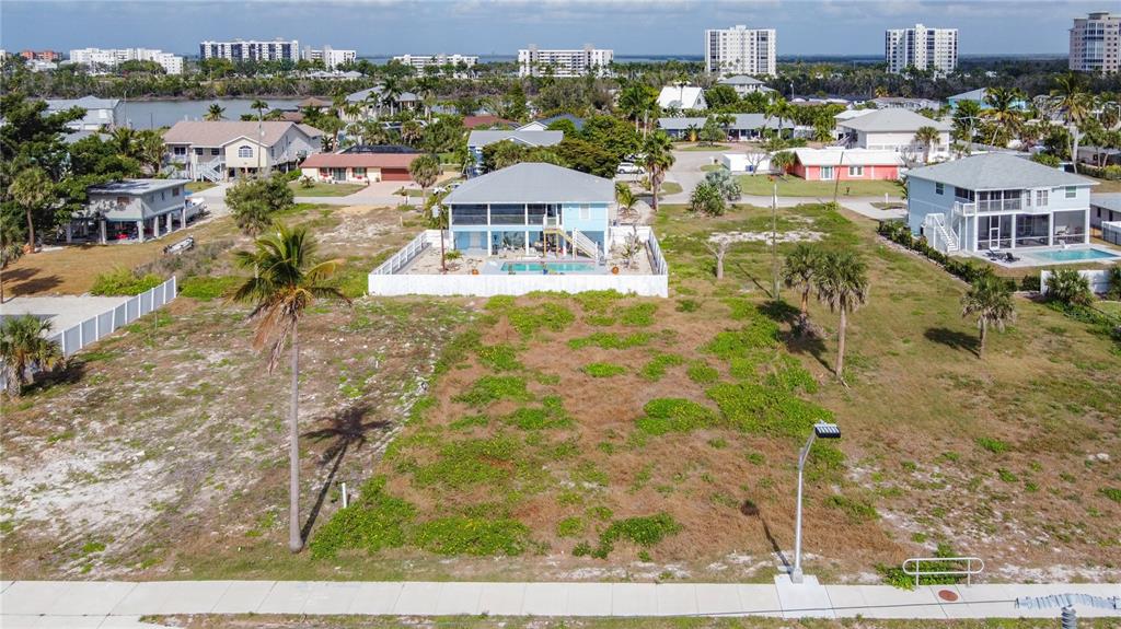 An aerial view shows a vacant, grassy lot in front of a light blue house — 8033 ESTERO BOULEVARD, FORT MYERS BEACH, FL