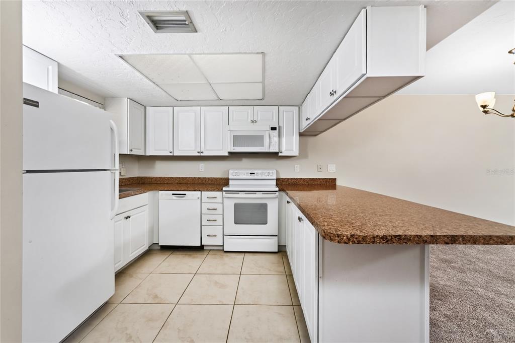 A kitchen with white cabinets, granite countertops, white appliances, and beige tile flooring — 179 BOUNDARY BOULEVARD UNIT 3, ROTONDA WEST, FL
