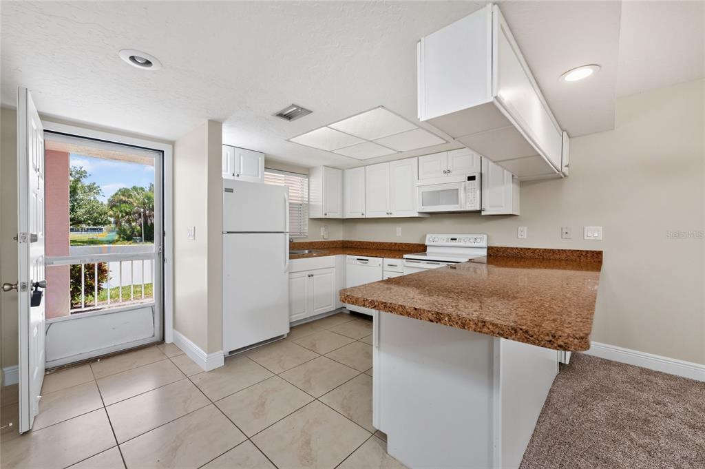 A kitchen with white cabinets, granite countertops, white appliances, and a tiled floor — 179 BOUNDARY BOULEVARD UNIT 3, ROTONDA WEST, FL