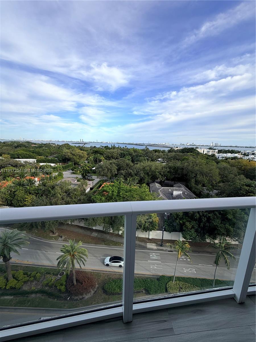A high-angle view from a balcony overlooking a road, lush trees, and a distant bay — 4250 Biscayne Blvd # 902, Miami FL 33137, MIAMI, FL