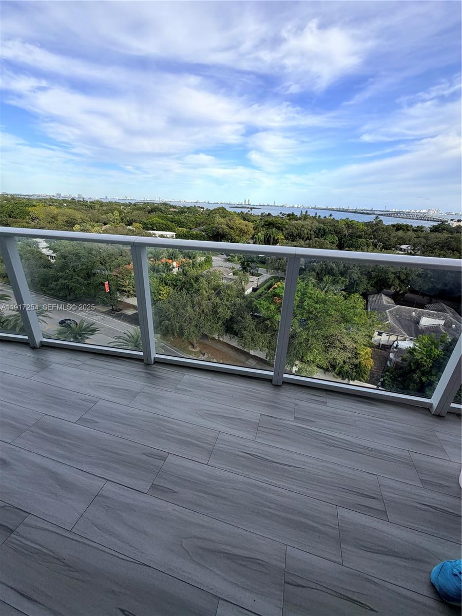 A balcony with wood-look tile flooring overlooks a lush green landscape and a distant bay — 4250 Biscayne Blvd # 902, Miami FL 33137, MIAMI, FL