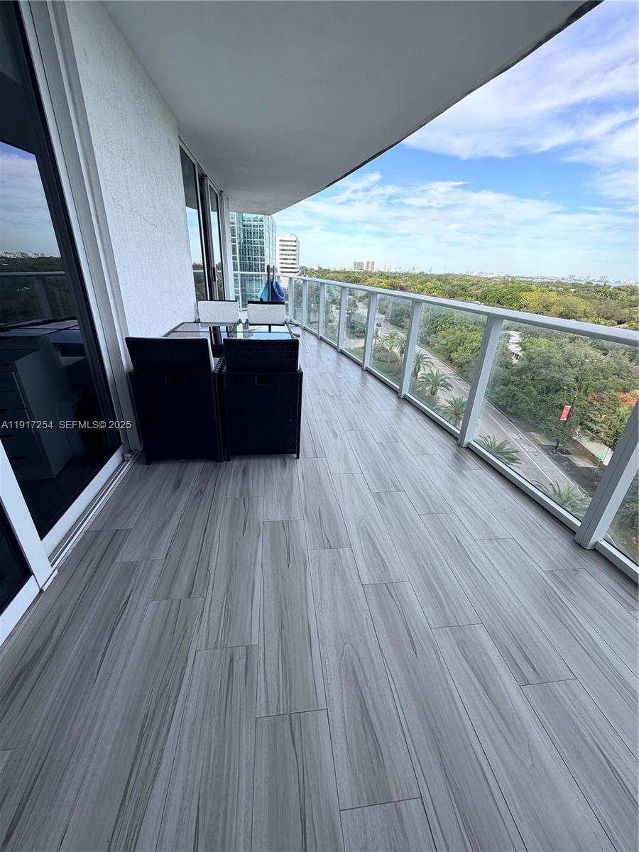 A balcony with wood-look tile flooring, outdoor seating, and a glass railing overlooking trees — 4250 Biscayne Blvd # 902, Miami FL 33137, MIAMI, FL