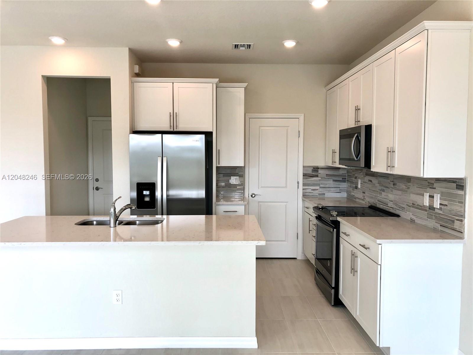 A modern kitchen features white cabinets, stainless steel appliances, and a quartz-topped island — 4984 Greenway Dr, Hollywood FL 33021, HOLLYWOOD, FL