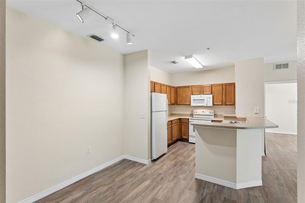 A kitchen with wood cabinets, white appliances, and a breakfast bar overlooking a dining area — 8136 CLAIRE ANN DRIVE UNIT 207, ORLANDO, FL