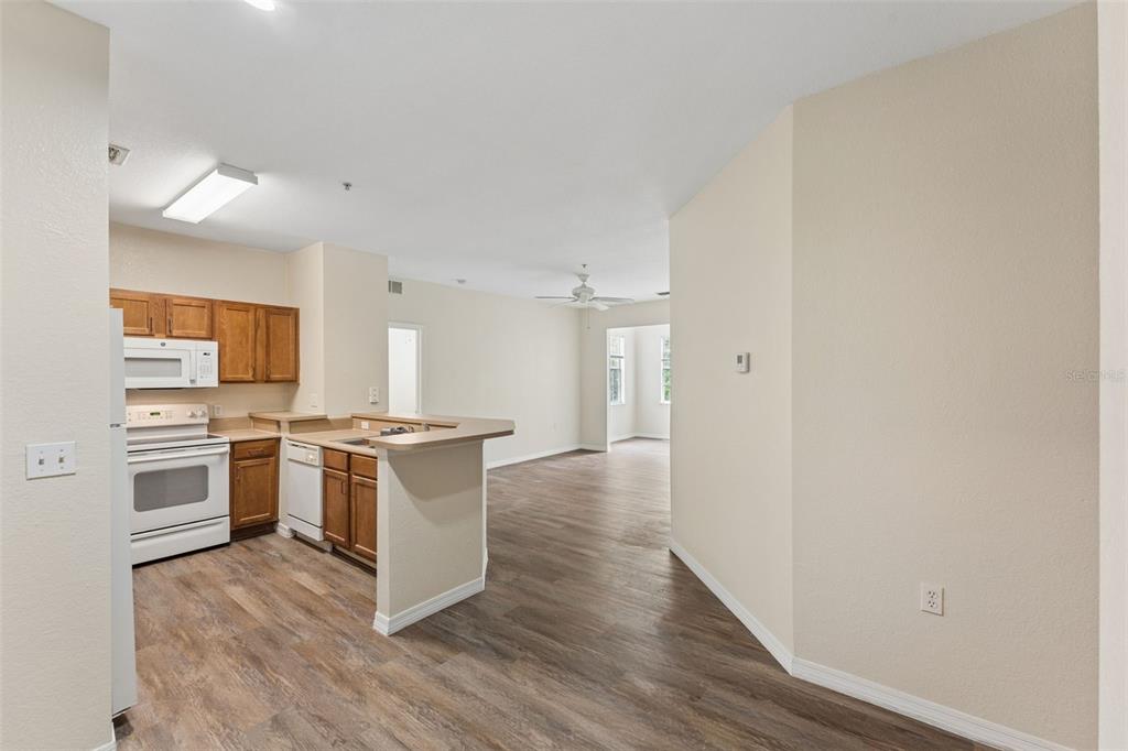 An open-concept kitchen with wood cabinets and a breakfast bar overlooks a living area — 8136 CLAIRE ANN DRIVE UNIT 207, ORLANDO, FL