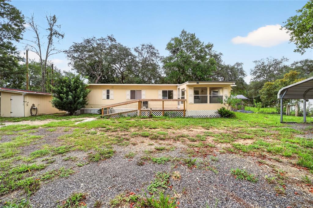 A light yellow mobile home with a wooden deck and ramp sits on a gravel lot — 15367 NE 160TH AVENUE ROAD, FORT MC COY, FL