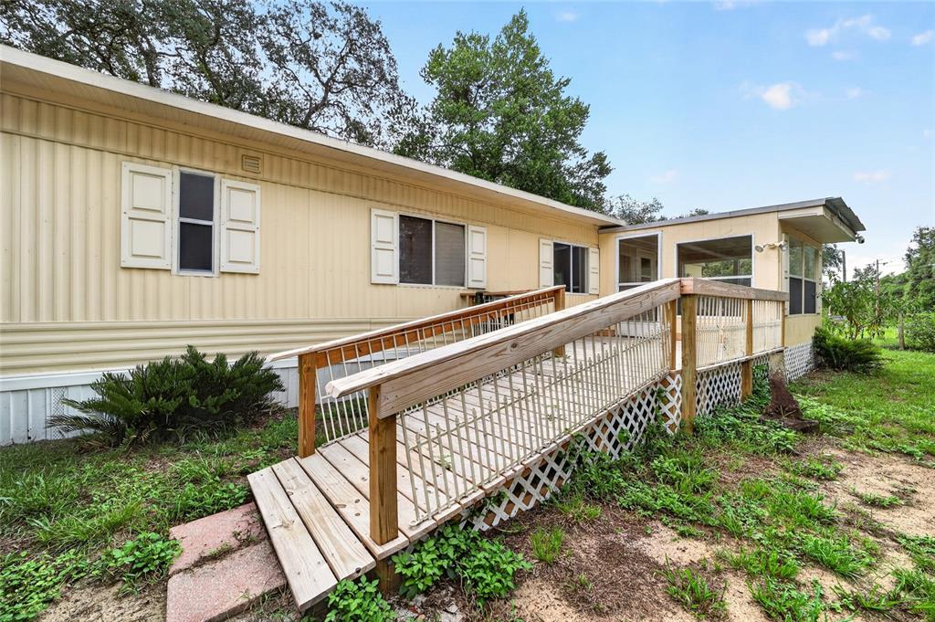 A mobile home exterior features a wooden wheelchair ramp leading to a screened-in porch — 15367 NE 160TH AVENUE ROAD, FORT MC COY, FL