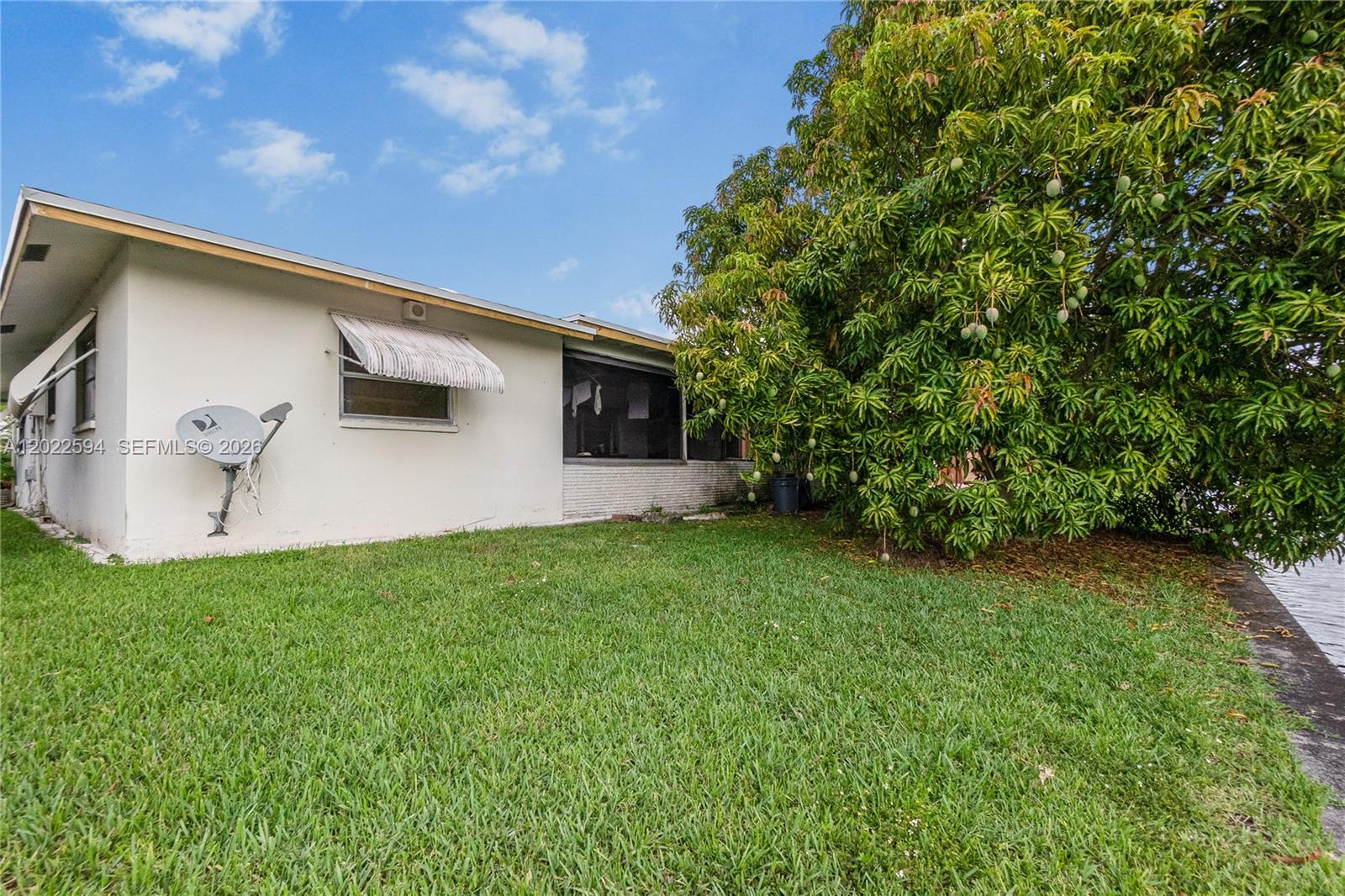 The exterior of a white house features a large mango tree and a satellite dish — 6013 NW 68th, Tamarac FL 33321, TAMARAC, FL
