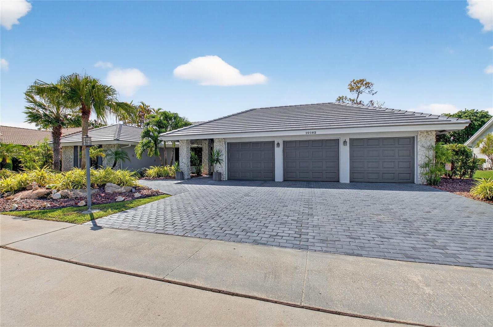 A single-story house with a three-car garage and a paved driveway under a blue sky — 10182 Boca Woods Lane, Boca Raton FL 33428, BOCA RATON, FL