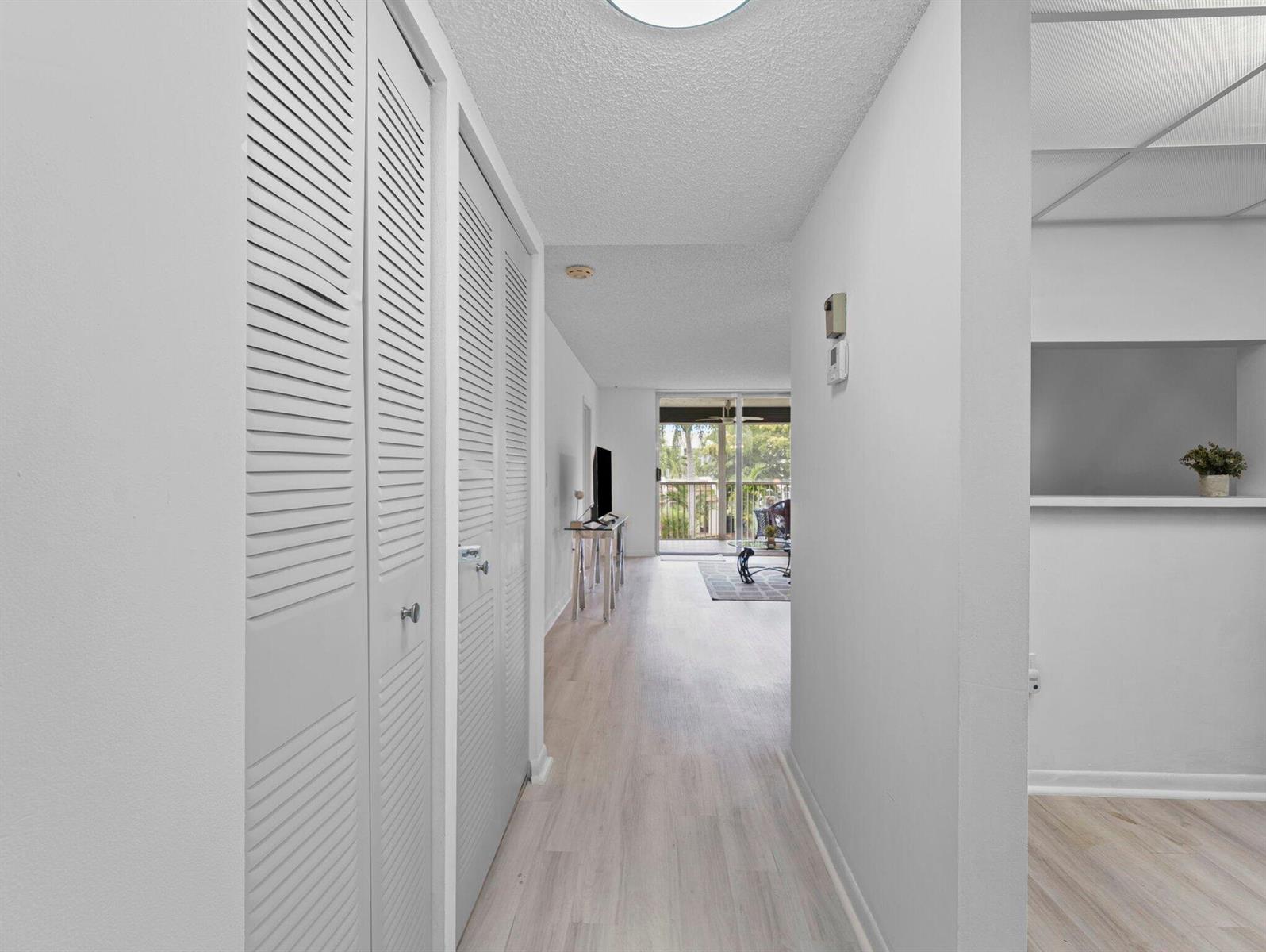 A hallway with louvered closet doors leads to a living area with a balcony view — 6800 Royal Palm Boulevard # 207f, Margate FL 33063, MARGATE, FL