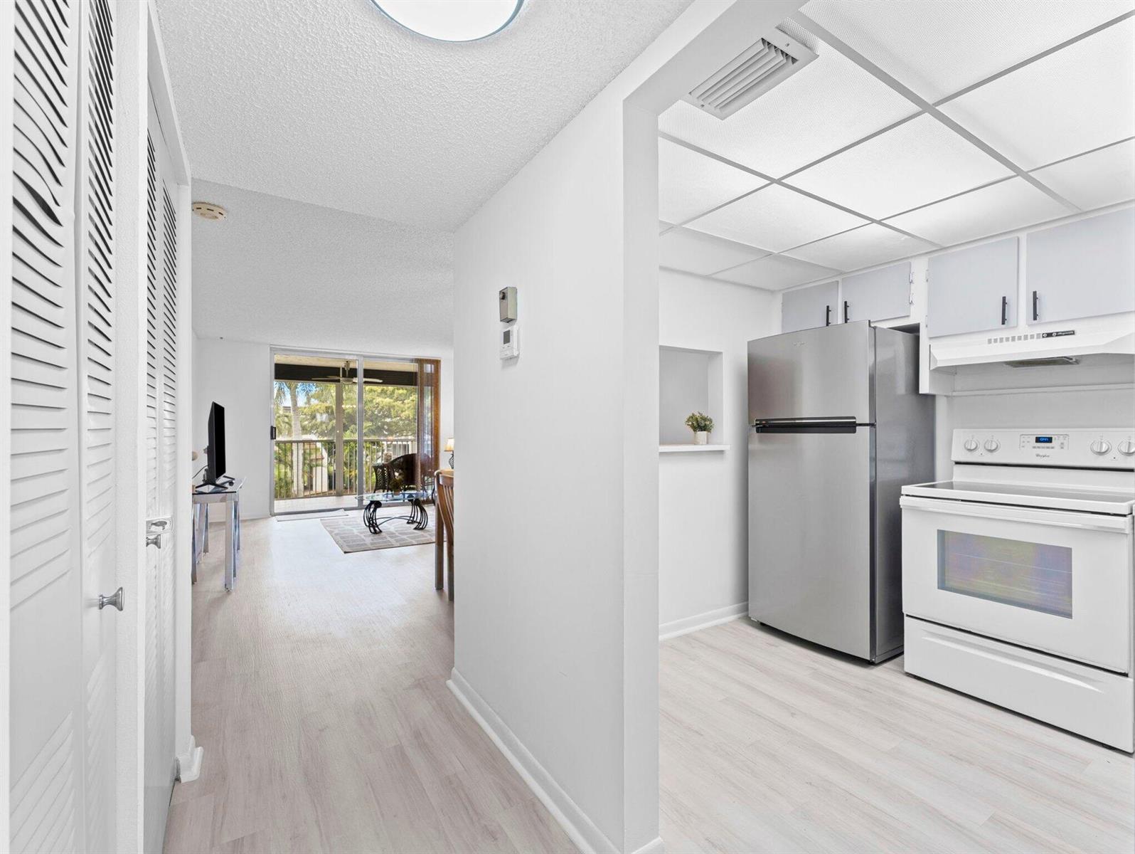 A view from a hallway into a kitchen with stainless appliances and an adjacent living area — 6800 Royal Palm Boulevard # 207f, Margate FL 33063, MARGATE, FL