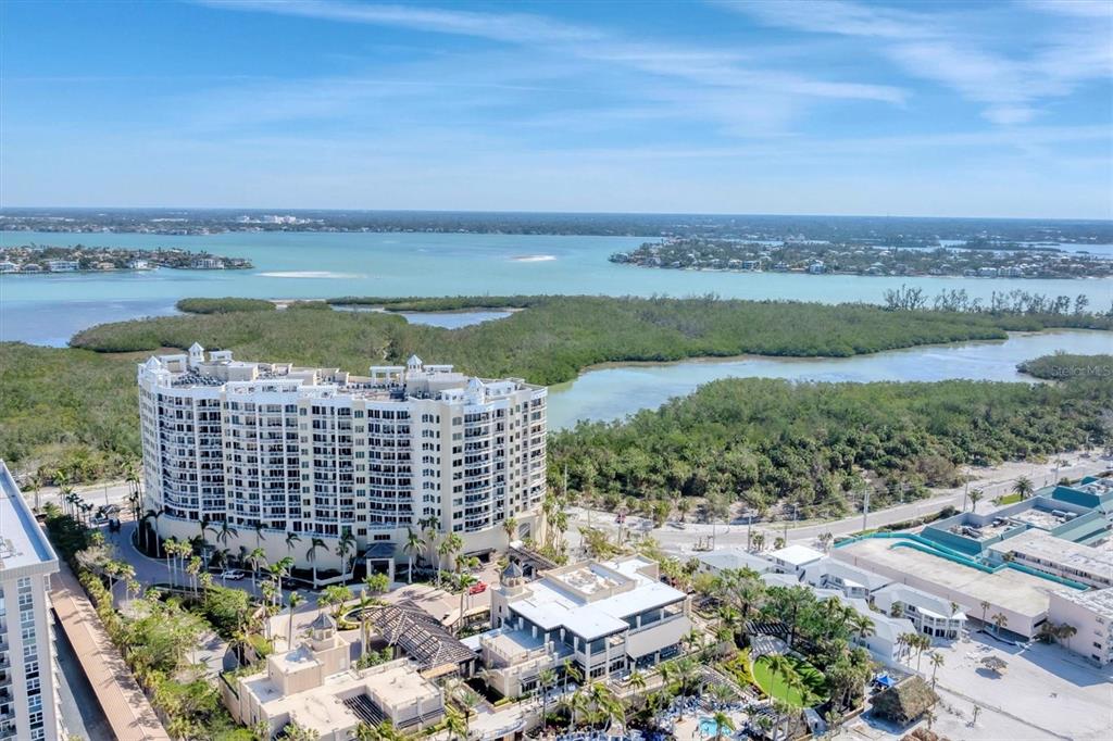 An aerial view shows a large multi-story residential building surrounded by lush vegetation and water — 1300 BENJAMIN FRANKLIN DRIVE UNIT 304, SARASOTA, FL
