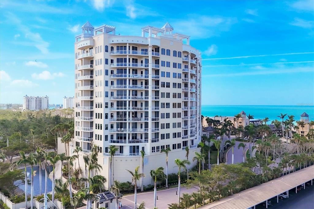 An aerial view of a tall, multi-story residential building near the ocean with palm trees — 1300 BENJAMIN FRANKLIN DRIVE UNIT 304, SARASOTA, FL