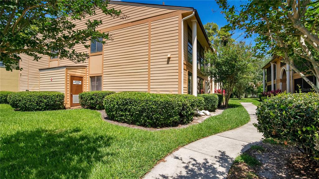 A two-story tan apartment building with horizontal siding, a concrete walkway, and manicured landscaping — 6019 SCOTCHWOOD GLEN UNIT 204, ORLANDO, FL
