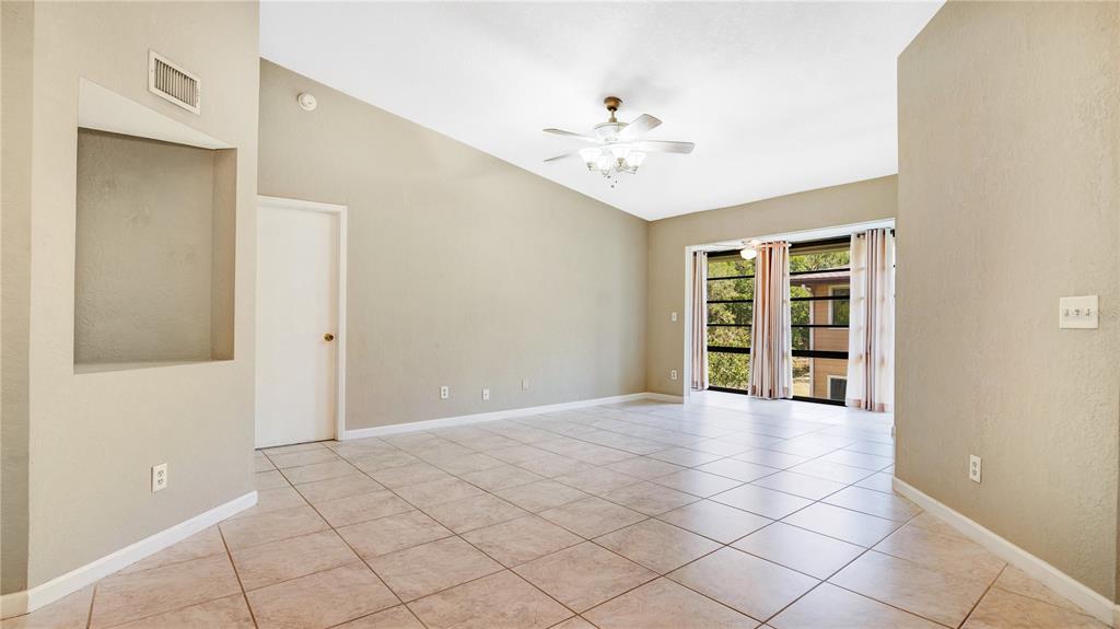 An empty living room features beige walls, tile flooring, a ceiling fan, and large windows — 6019 SCOTCHWOOD GLEN UNIT 204, ORLANDO, FL