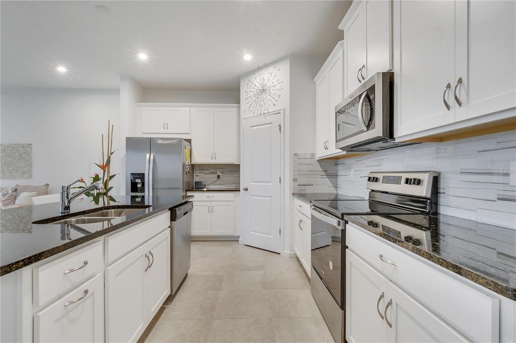 A modern kitchen features white cabinets, stainless steel appliances, dark countertops, and light tile flooring — 1098 BOARDWALK PLACE, KISSIMMEE, FL