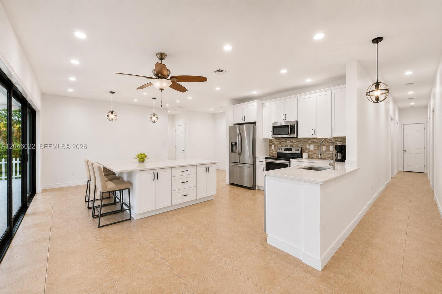 A modern kitchen features white cabinetry, stainless steel appliances, a large island, and tile flooring — 26363 SW 152nd Ave, Homestead FL 33032, HOMESTEAD, FL